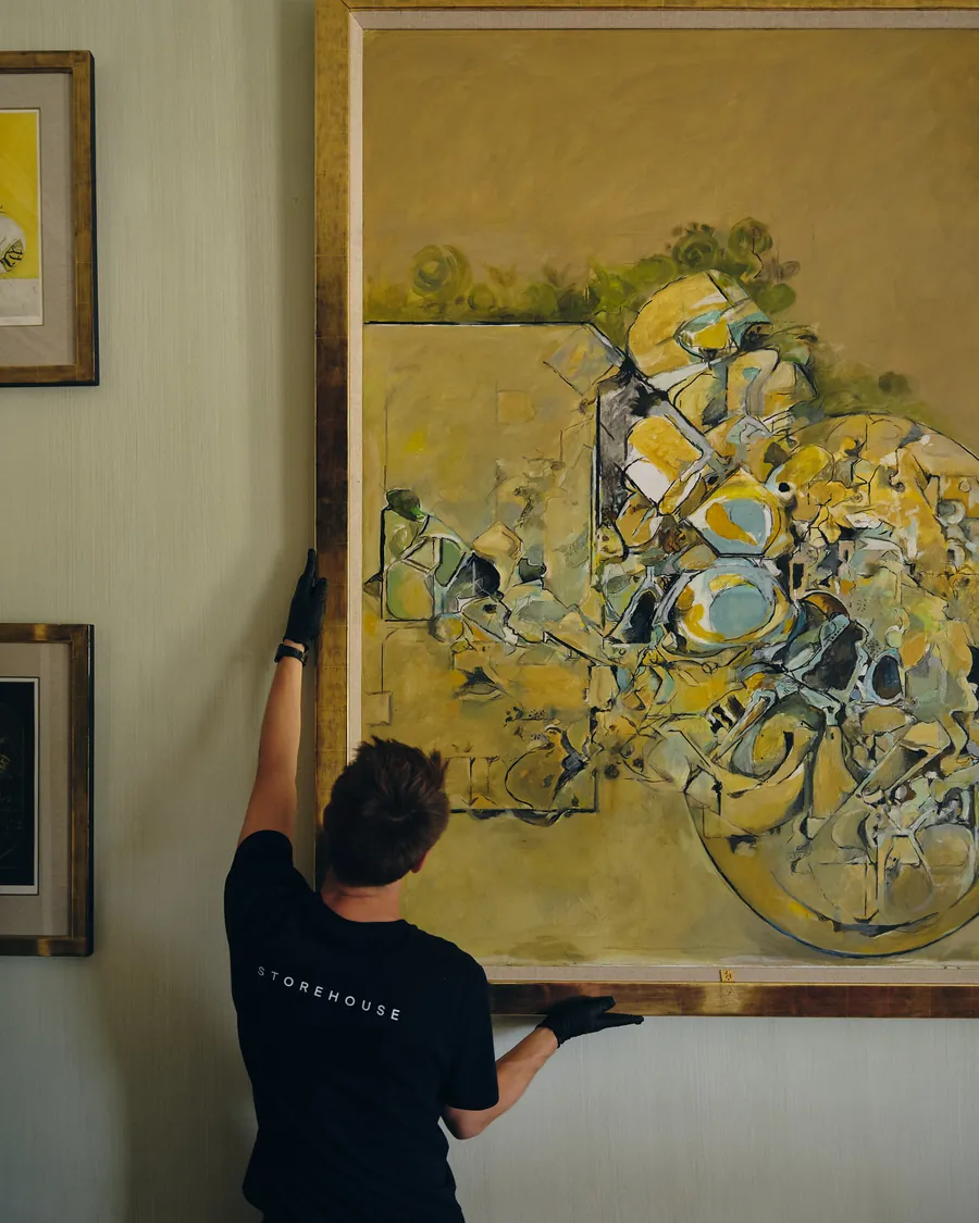 A technician hanging a large painting on a gallery wall.