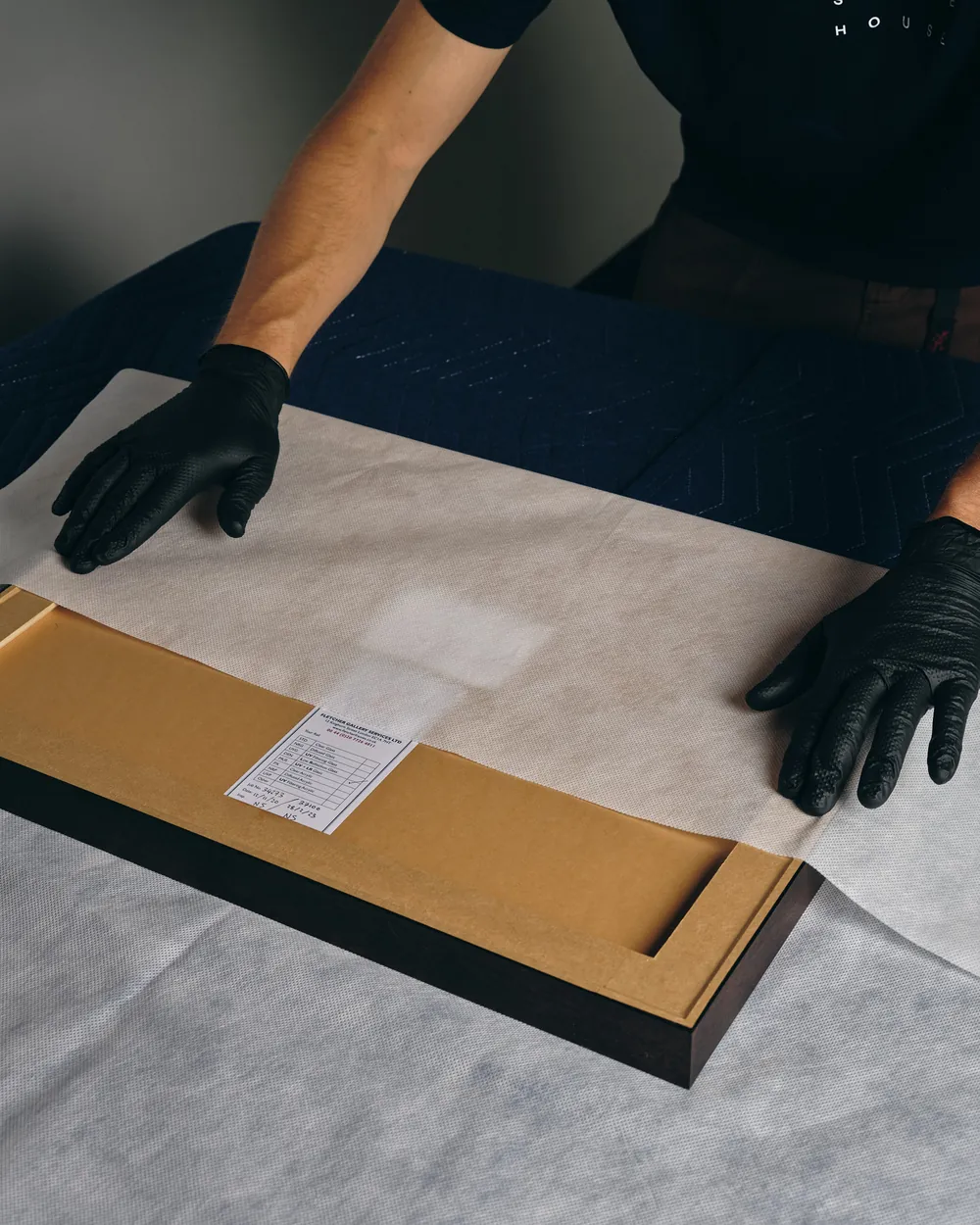 A framed work laid face-down on a padded table with its paperwork beside it.