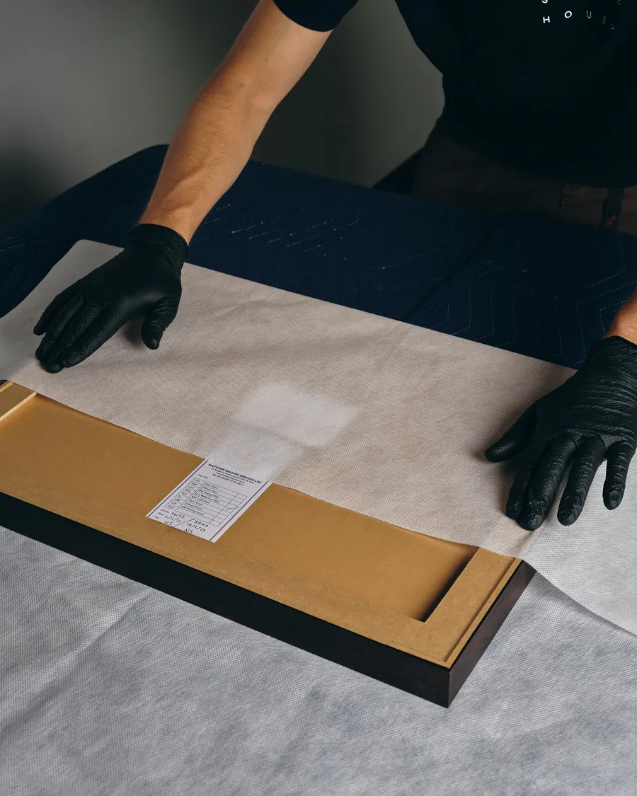 A framed work laid face-down on a padded table with its paperwork beside it.