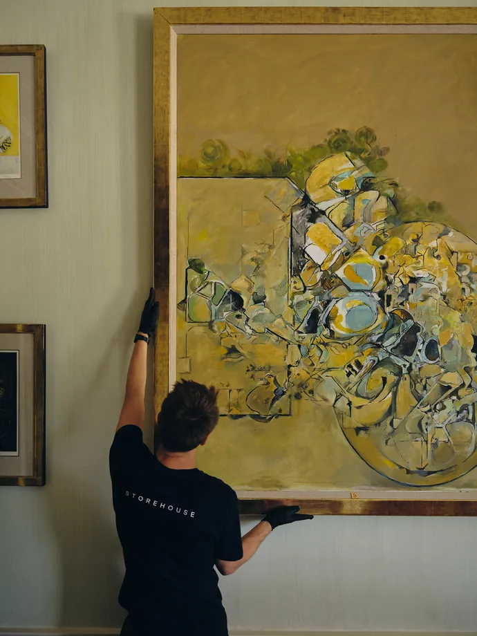 A large painting being hung on the wall of an interior.