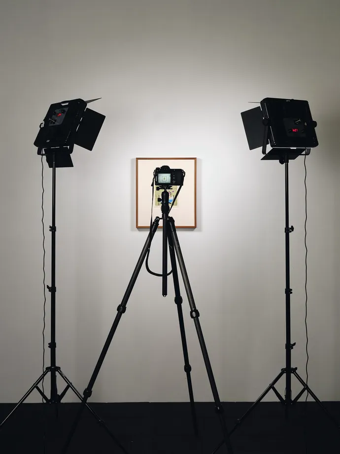 A framed work lit by two studio lights, with the camera on a tripod between them.