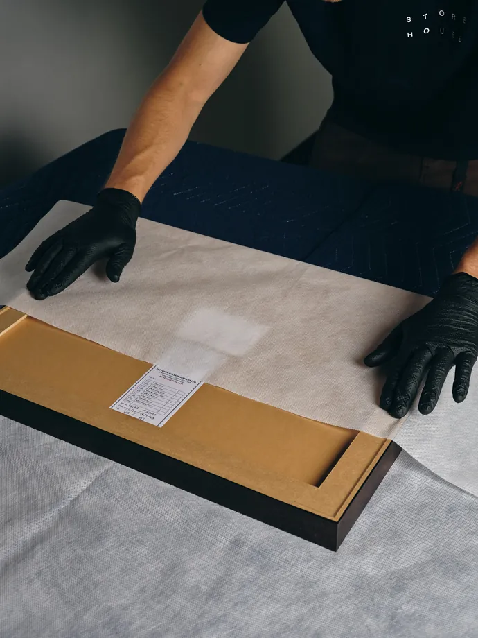 A framed work laid face-down on a padded table with its paperwork beside it.