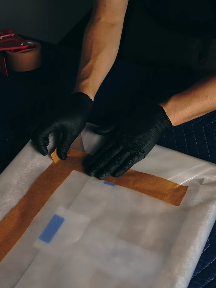 Gloved hands taping a wrapped work closed.